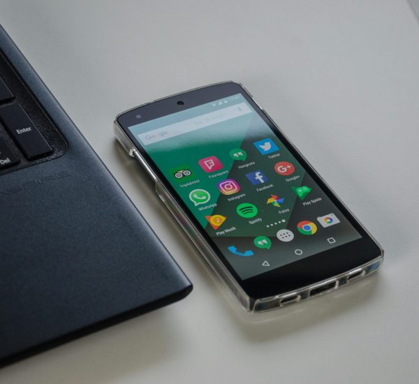 Smartphone on a table showing various social media apps beside a laptop keyboard.